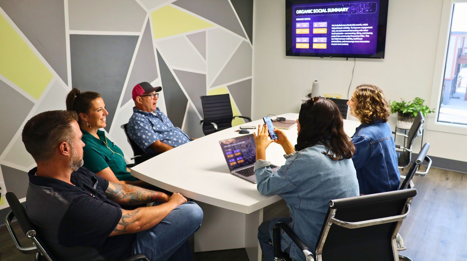 Five people in a meeting room looking at a screen showing an organic social summary report.